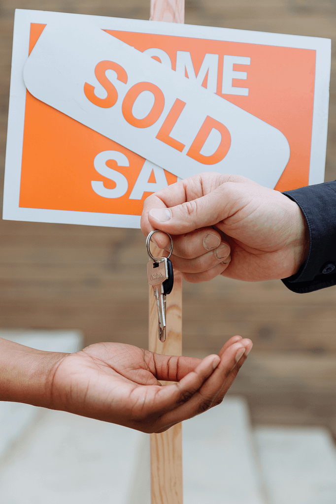 A photo of a hand holding keys with a sold sign over a for sale sign